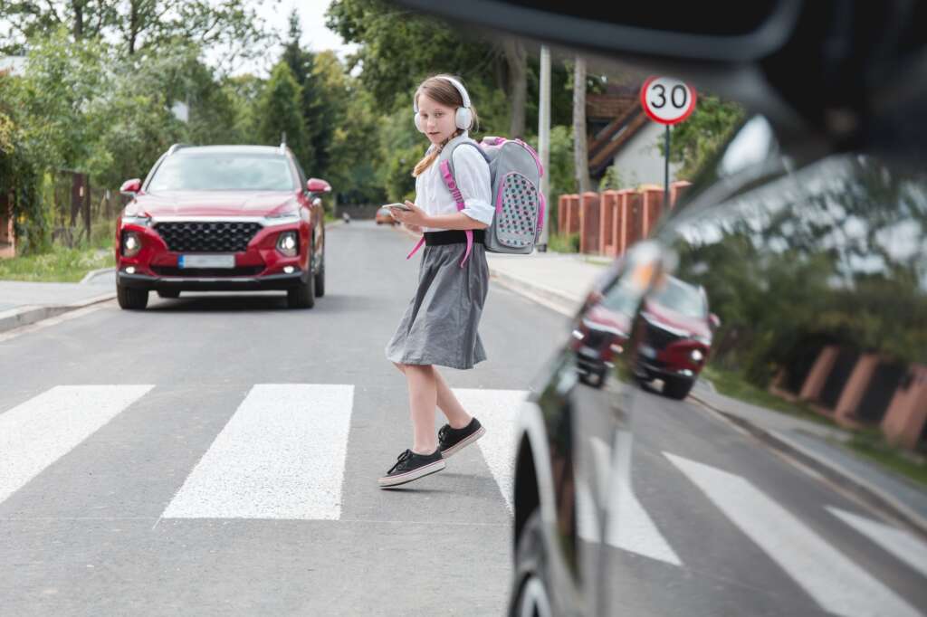 Испуганная девушка с телефоном и наушниками убегает от машины на пешеходном переходе